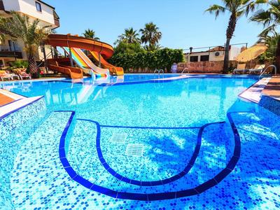 Bright blue swimming pool with water slide, surrounded by lounge chairs and palm trees under a blue sky.