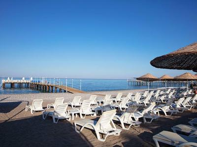 Empty beach with white lounge chairs, umbrellas, and a pier over clear blue sea.