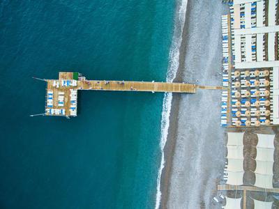 Aerial view of a pier with sun loungers and blue sea at a pebble beach