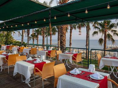 Restaurantterrasse mit gedeckten Tischen, Stühlen, Palmen und Meerblick bei Abendlicht.
