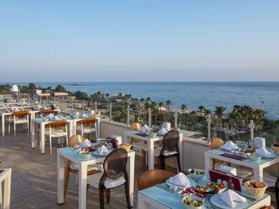 Dachterrasse mit gedeckten Tischen, Stühlen und Blick auf das Meer bei klarem Himmel.