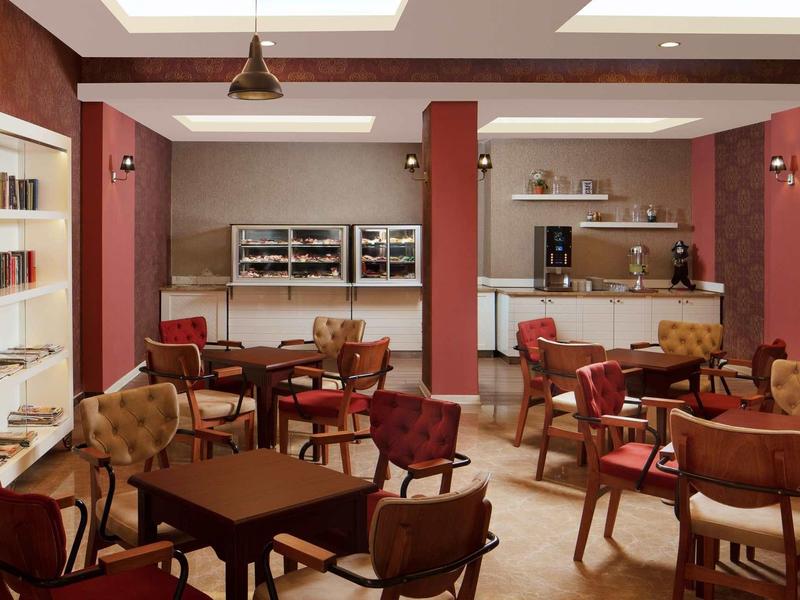 Gemütliches Cafe mit hölzernen Tischen, gepolsterten Stühlen und Bücherregalen an der Wand.