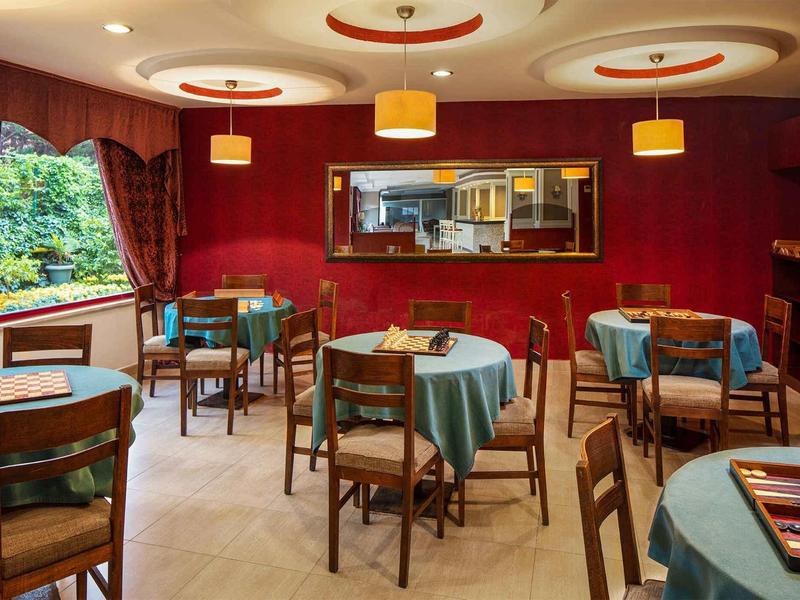 Gemütlicher Gastraum mit runden Tischen, blauen Tischdecken und Holzstühlen, rote Wände.