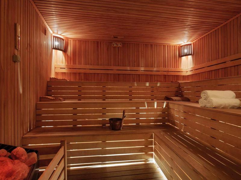 Sauna aus hellem Holz mit mehrstufigen Bänken, Handtüchern und weicher Beleuchtung.