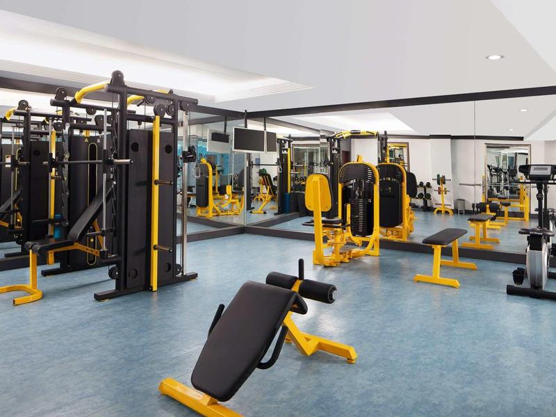 Moderner Fitnessraum mit gelben Trainingsgeräten, Spiegelwänden und grauem Bodenbelag.