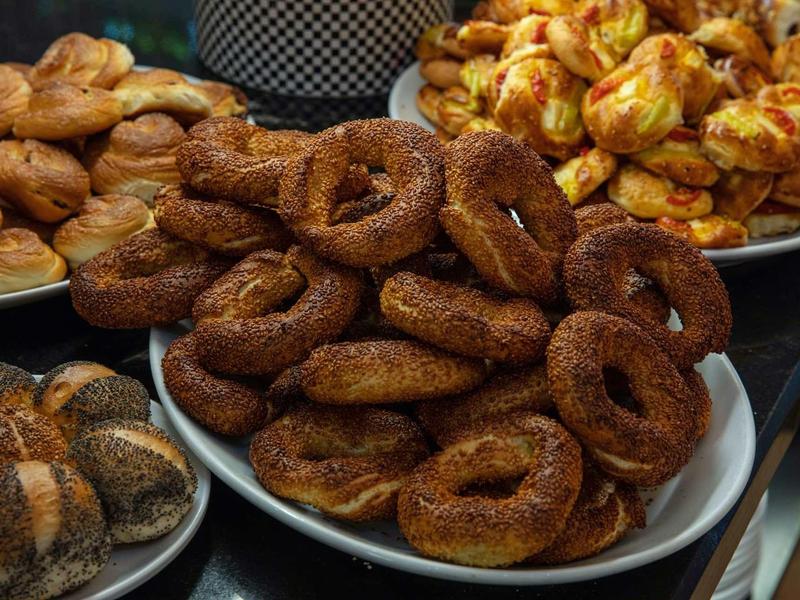 Verschiedene Arten von frisch gebackenem Gebäck, darunter Simits, Brötchen und Sesamringe, auf Tellern.