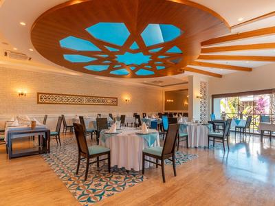 Ristorante elegante con tavoli rotondi e rettangolari, pavimento in legno e soffitto decorativo.