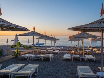 Lettini e ombrelloni vuoti sulla spiaggia al tramonto con vista sul mare calmo.