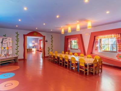 Una stanza luminosa e colorata con un lungo tavolo, sedie e finestre decorative.