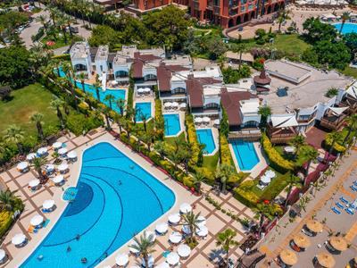 Vista de un resort con piscinas y tumbonas, rodeado de paisaje verde y edificios.