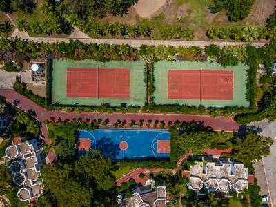Tres canchas deportivas al aire libre, dos de tenis y una de baloncesto, rodeadas de árboles y edificios.