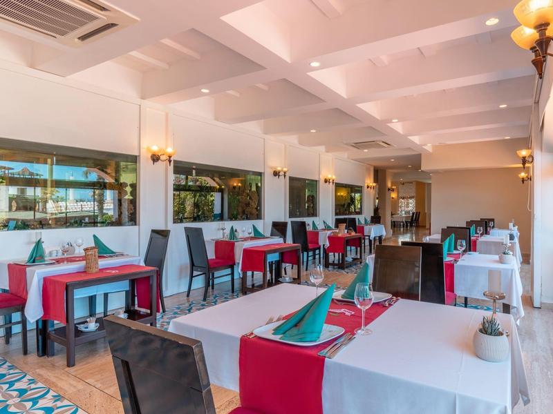 Ristorante luminoso con tavoli bianchi, sedie rosse e grandi finestre con vista sulla piscina.