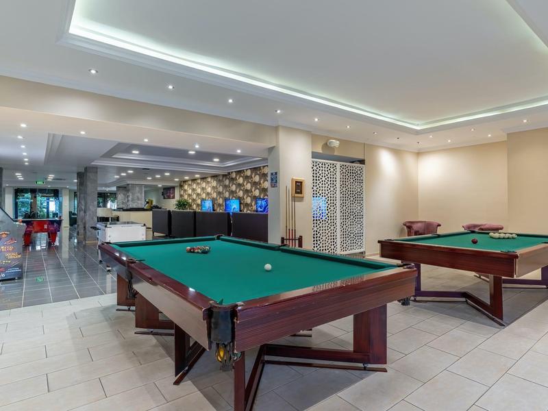 Due tavoli da biliardo in una sala giochi ben illuminata di un hotel con area salotto sullo sfondo.