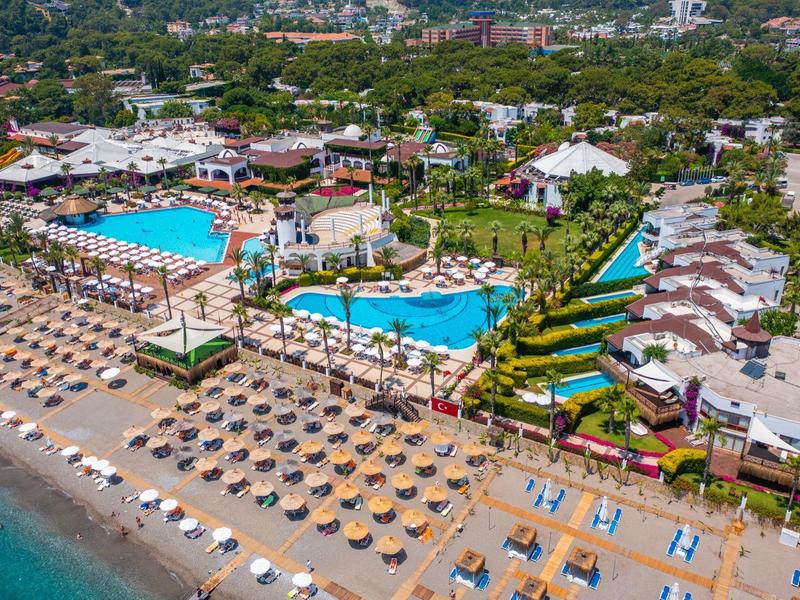 Vista aerea di una spiaggia con lettini, piscine e edifici dell'hotel in un resort per vacanze.