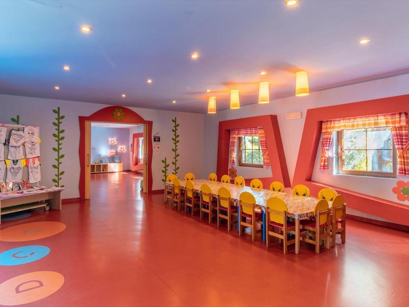 Una stanza luminosa e colorata con un lungo tavolo, sedie e finestre decorative.