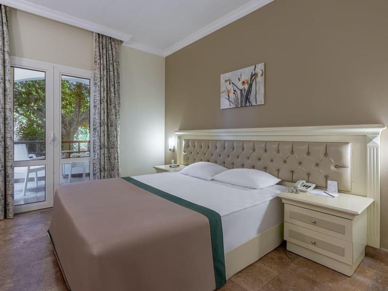 Camera d'hotel moderna con letto matrimoniale, comodini e accesso al balcone con vista sul giardino.