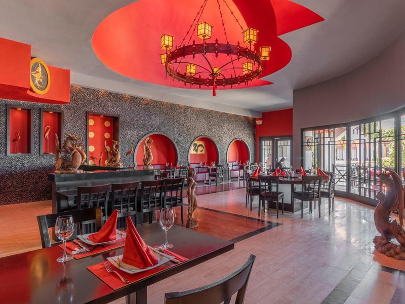 Ristorante d'hotel elegante con decorazioni rosse e grigie, lampadario decorativo e grandi finestre.