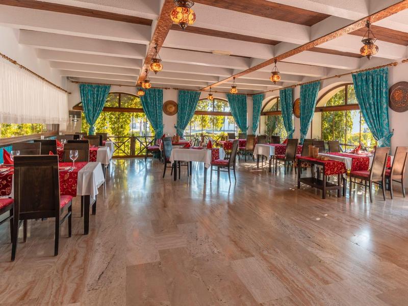 Ristorante luminoso e spazioso con soffitto a travi in legno e grandi finestre, decorato con tende verdi.