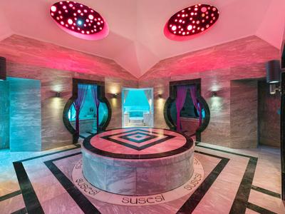 Hammam turc moderne avec fontaine centrale en marbre, murs élégants et éclairage coloré.