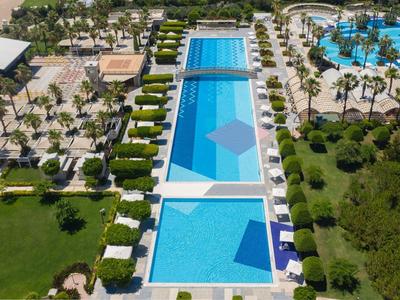 Großer Poolbereich mit mehreren rechteckigen Pools, grünen Rasenflächen und Palmen in einem Resort.