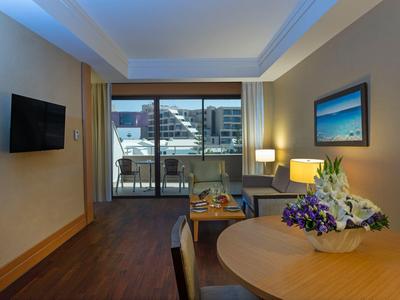 Chambre d'hôtel moderne avec balcon, table ronde et télévision murale.