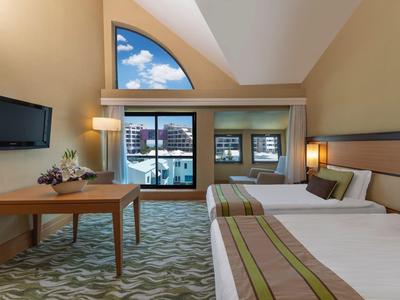 Chambre d'hôtel avec deux lits, bureau et grandes fenêtres avec vue sur la ville.