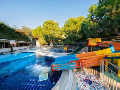 Une aire de toboggans aquatiques colorés à côté d'une piscine dans un jardin d'hôtel entouré d'arbres.