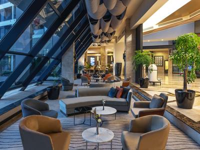 Moderner Hotel-Loungebereich mit bequemen Sesseln und Sofas unter einer Glasfront.