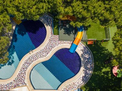 Luftaufnahme eines Schwimmbeckens mit Wasserrutsche und umgeben von Bäumen in einem Hotelresort.