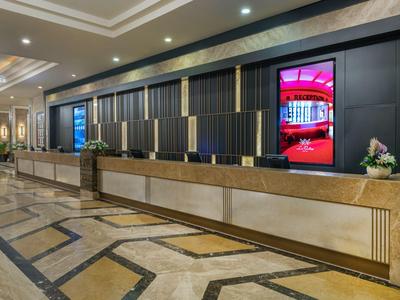 Moderner Hotel-Empfangsbereich mit langem Tresen und digitaler Anzeigewand.