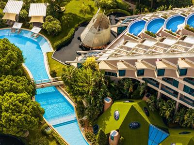 Luftaufnahme eines luxuriösen Hotels mit schwimmenden Pools, grüner Landschaft und modernen Gebäuden.