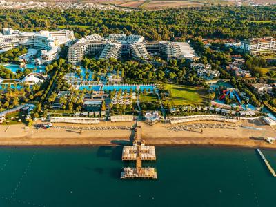 Luftaufnahme eines Hotelkomplexes mit Schwimmbädern, Strand und Steg am klaren blauen Meer.