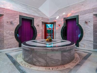 Moderner Spa-Raum mit rundem Marmorbecken und kugelförmigen Türen vor violetten Vorhängen.