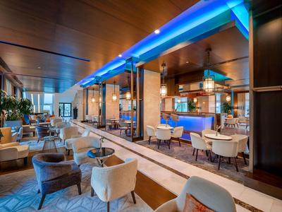 Modernes Hotelrestaurant mit blau beleuchteter Bar, bequemen Stühlen und eleganter Holzdecke.