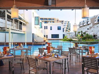 Terraza de hotel con mesas y sillas frente a una gran piscina en un complejo moderno.