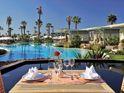 Una mesa puesta junto a la piscina de un hotel con palmeras y cielo azul despejado.