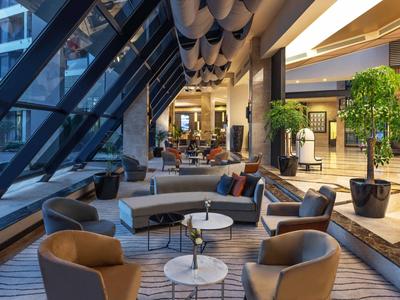 Moderna recepción de hotel con áreas de descanso, grandes ventanales y plantas.