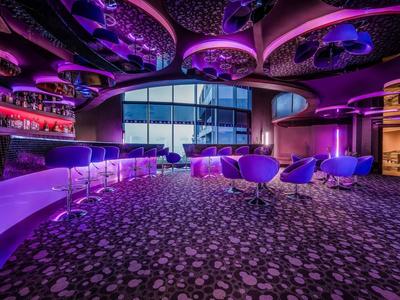 Bar moderno de hotel con iluminación púrpura, luces de techo redondas y sillones cómodos.