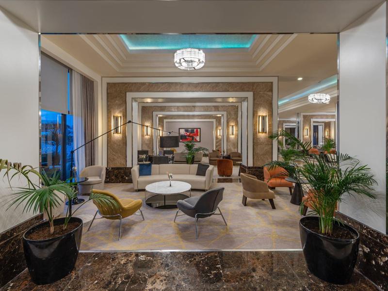 Lobby d'hôtel élégante avec espaces de sièges stylés, plantes vertes et éclairage moderne.