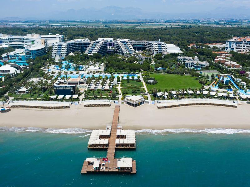 Grand complexe balnéaire avec piscines, transats et jetée vers la mer.