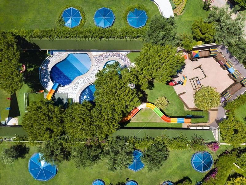 Vue aérienne d'un hôtel avec piscine, parasols et espaces verts.