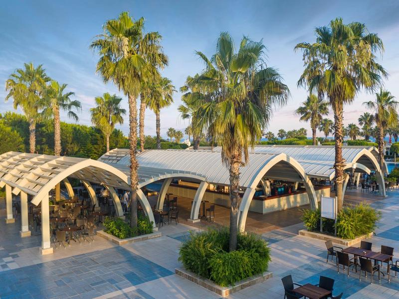 Restaurant en plein air moderne avec toits courbés et palmiers sur la plage de l'hôtel.