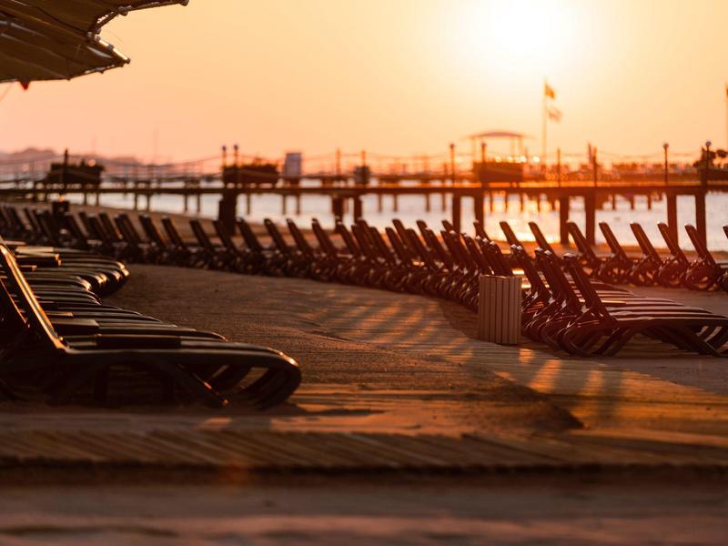 Chaises longues vides sur la plage au coucher du soleil avec un ciel orange doux.