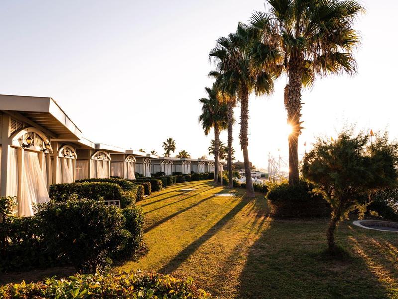 Bungalows alignés à côté de palmiers et pelouse au coucher du soleil.