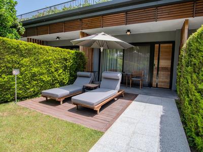 Due sdraio con ombrellone su terrazza di legno accanto a giardino e casa moderna