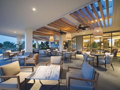 Moderne buitenruimte van een hotel met stijlvolle zitplaatsen en plafondventilatoren bij schemering.