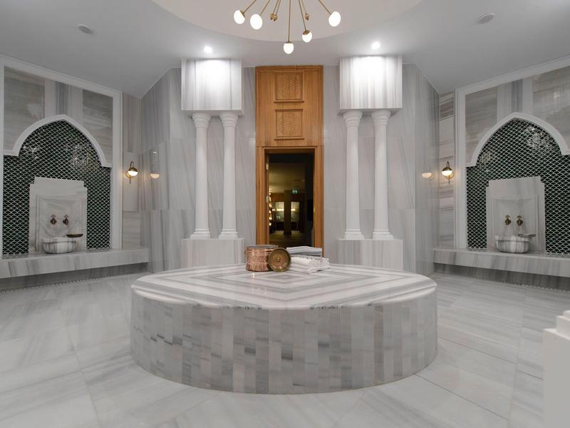 Spa luminosa con fontana centrale in marmo e bacini d'acqua simmetrici in una stanza lussuosa.