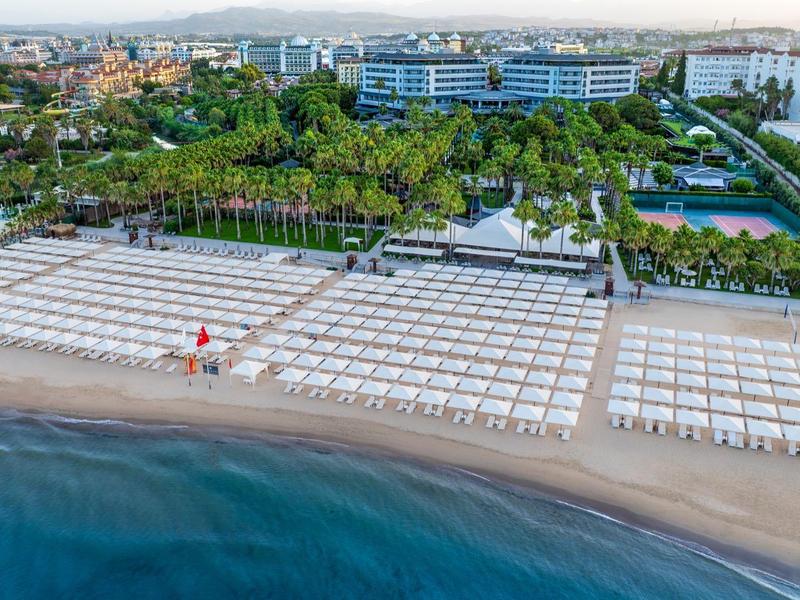 Vista di una grande area spiaggia organizzata con lettini davanti a un complesso alberghiero e molto verde.