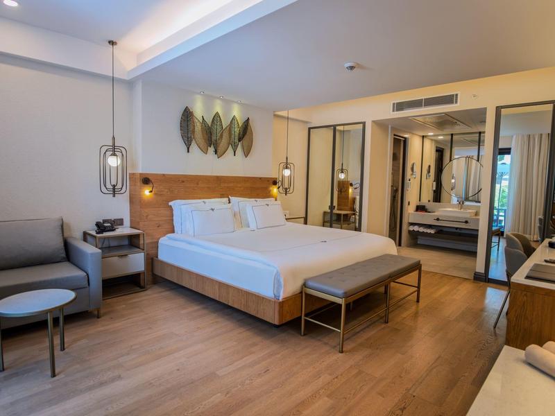 Camera d'hotel moderna con letto grande, area salotto e parete a specchio.