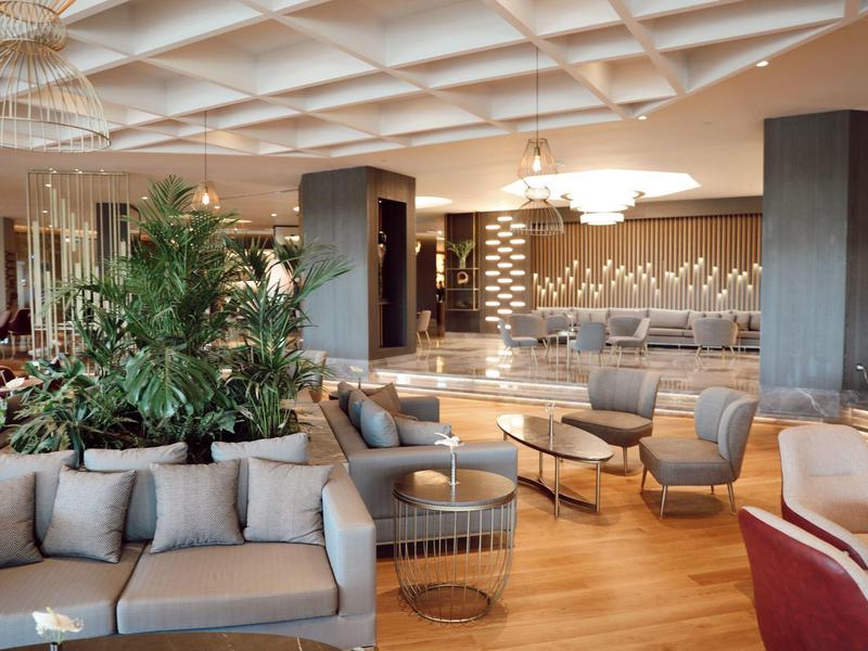 Luminosa hall d'hotel con area salotto moderna e piante su pavimento in legno.